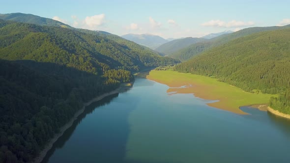 Aerial View of Big Lake with Clear Blue Water Between High Mountain Hills Covered with Dense alt