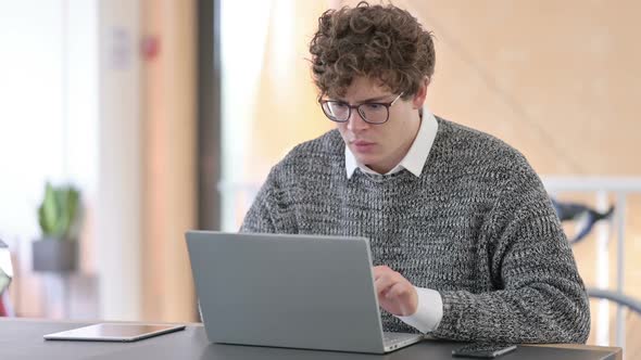 Young Man Reacting to Loss on Laptop at Work alt