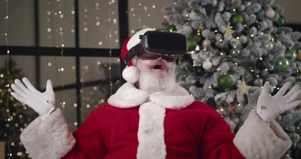 Curious Elderly Charming Caucasian Man in Santa Claus Carnival Costume Puts on VR Glasses and alt