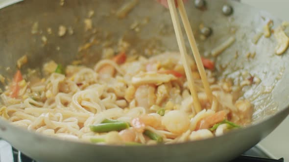 Woman stirring hot wok noodles with chopsticks alt