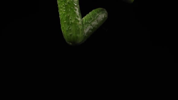Three Juicy Cucumbers Fly Up Spinning and Fall on a Black Background in Slow Motion Shot alt