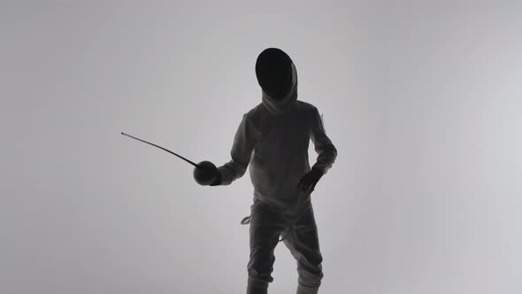 Silhouette of Young Boy in White Uniform and Mask Masterfully Wields Rapier on Gray Studio alt