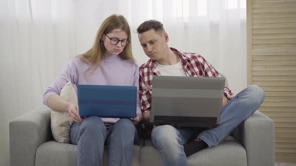 Young Redhead Millennial Woman in Eyeglasses Asking Boyfriend for Help with Laptop alt