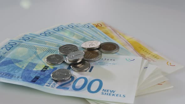 New Israeli Shekels bills and coins rotating on a reflective surface alt