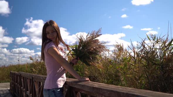 Happy Nice Fun Girl in Pink T-shirt Look in Camera with Reed in Her Hand. Then Hide From Camera alt