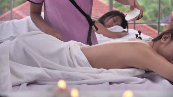 The massage therapist is pouring aroma essential oil skincare on the back of young Asian woman alt