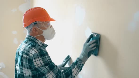 An Elderly Man Master Levels a Wall with a Tool in an Orange Helmet and Protective Glasses While