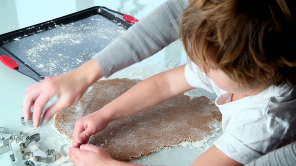 Mom and Son Roll Out Dough and Cut Gingerbread Cookie Figurines Together in the Kitchen alt