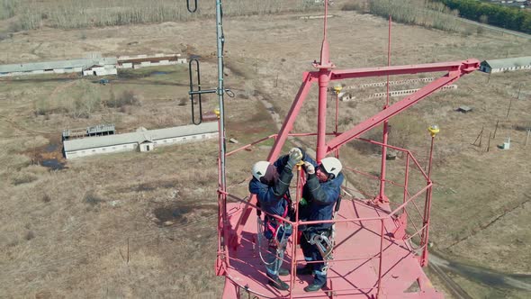 Two Industrial Climbers in Helmets and Gear Repair Lighting Lamps on Communication Mast