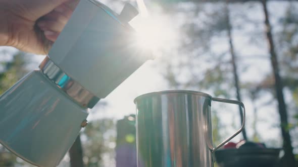 A Woman's Hand Pours Fresh Coffee From a Geyser Coffee Maker Into a Steel Mug in Nature Against the alt