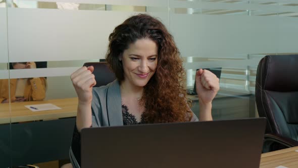 Happy woman feeling excited looking at laptop screen sitting at workplace being promoted. alt