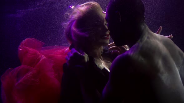 Man and Woman Are Floating Underwater, Hugging and Looking To Each Other with Love alt