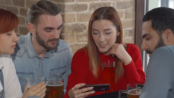 Young People Using Smart Phone While Drinking Beer Together at the Pub alt