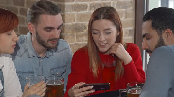 Young People Using Smart Phone While Drinking Beer Together at the Pub
