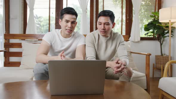 Happy young asian gay couple sit couch use smartphone facetime video call with friends and family.