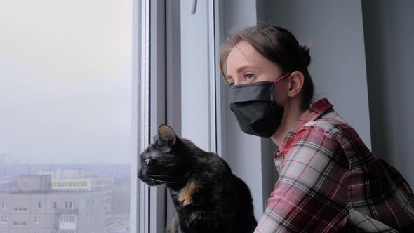 Slow Motion: Woman in Medical Face Mask and Black Cat Looking Out of Window