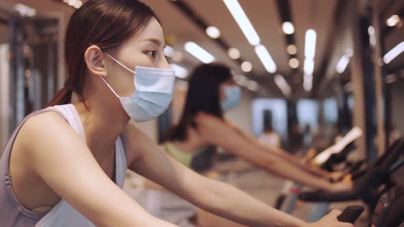Young  asian female  in sport wear outfit in gym  with medical protective mask alt