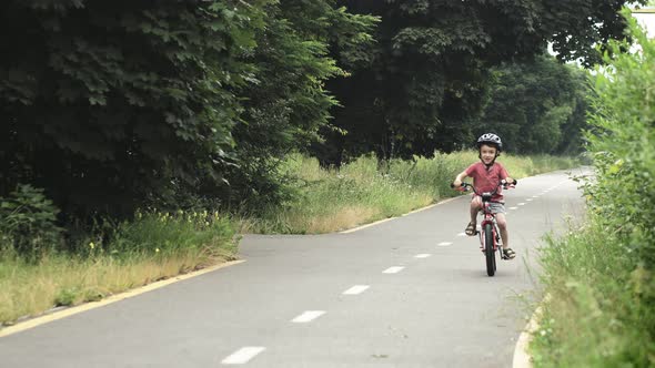 Child riding bicycle on the bike path at rain. Kid in helmet learning to ride at summer. alt
