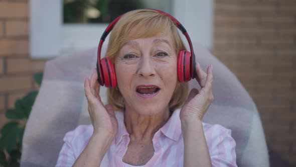 Headshot Portrait of Joyful Senior Caucasian Woman in Headphones Singing Looking at Camera Smiling alt