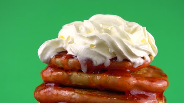 Pancakes with strawberry topping and whipped cream on a green background. alt