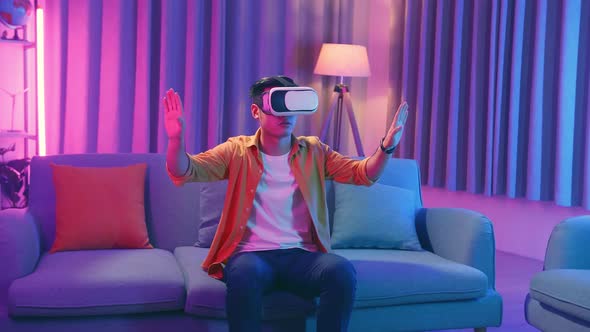 Young Asian Man Wearing Vr Headset At Living Room, Using Hand Touching And Slide alt