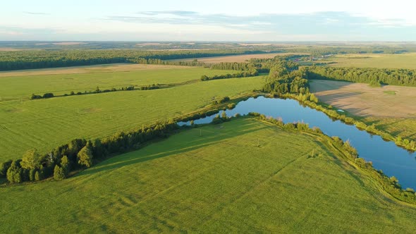 Aerial Top View of Grassy Furrowed Field. Fertile Meadow and Pound in Spring Day alt