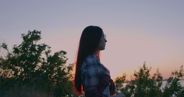 Young girl on the background of sunset looks into the distance alt