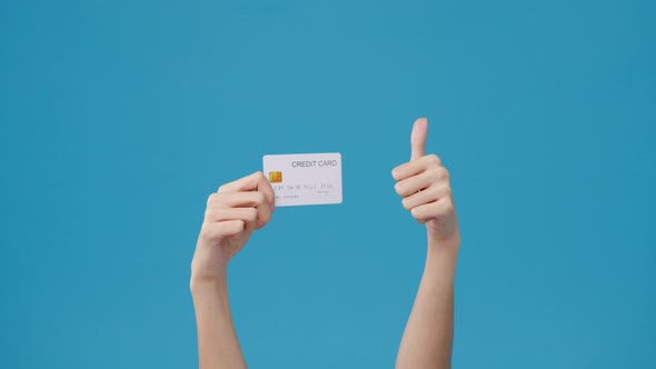 Young girl hold in hand credit bank card showing thumb up isolated over blue background in studio.