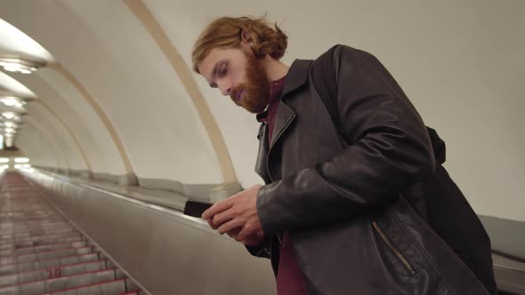Man Using Smartphone while Standing on Moving Staircase alt