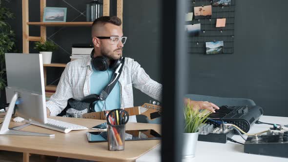 Attractive Young Man Playing Keyboard and Guitar Recording Music Indoors in Apartment alt