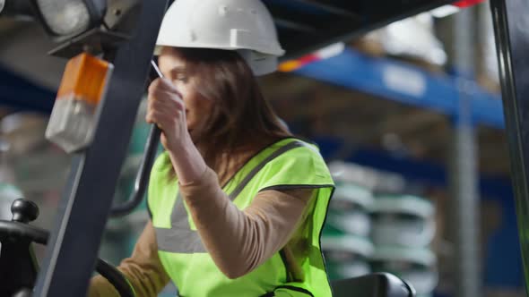 Live Camera Follows Confident Female Driver Autoloader Operator Sitting in Warehouse Forklift alt
