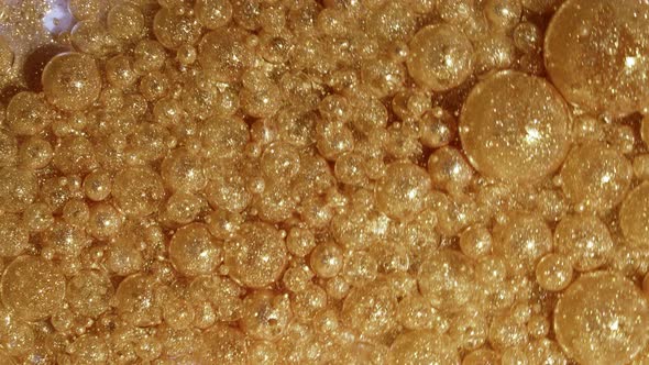 Abstract of Gold Pearl Bubbles Rotating and Bursts in White Glitter Paint alt