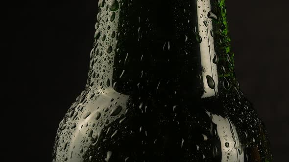 Drop of condensation drips on beer bottle glass. Water drops falling down