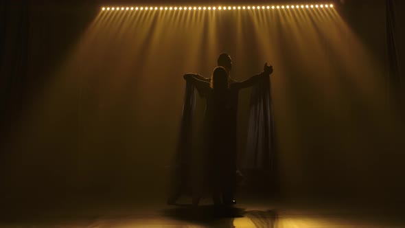 A Young Woman in a Long Dress and a Man in a Tuxedo Are Dancing a Waltz. Shot in a Dark Studio alt