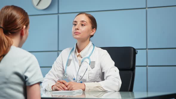 Young woman doctor in white coat examines hospital visitor alt