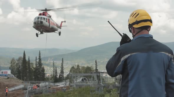 A Construction Engineer on a Walkie-talkie Commands a Cargo Helicopter Raises the Building Structure