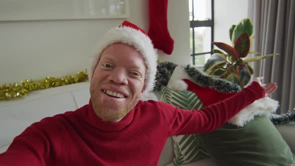 Happy albino african american man wearing santa hat making video call at christmas alt