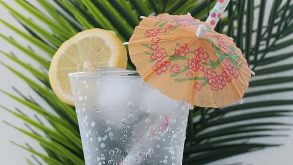 Soda Water With Lemon And Ice Cubes And Cocktail Umbrella Rotating
