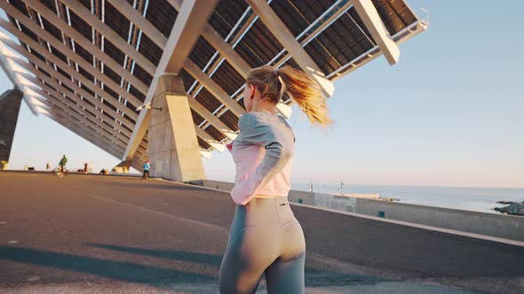 Millennial Female Jogging By Embankment Area of Modern Coastal City alt