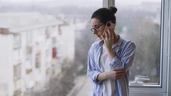 Woman with Glasses Talks on Phone Near Window