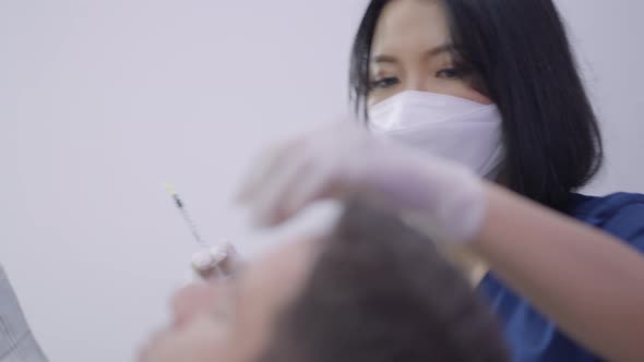 Young Concentrated Doctor Cleaning Patients Forehead Before Applying Collagen Injection alt