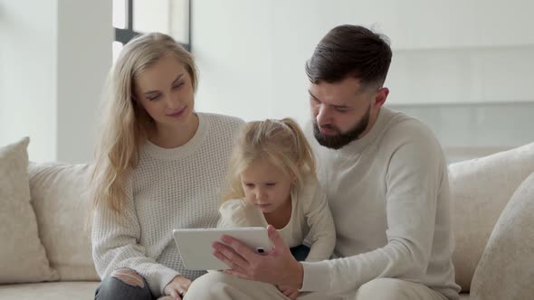 Young Family is Sitting on the Couch and Using a Tablet Watching a Movie or Surfing the Internet alt