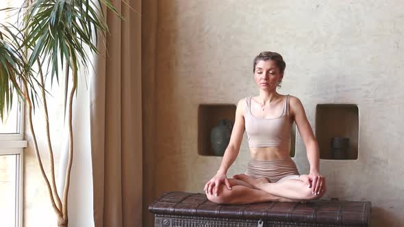 A Slender and Beautiful Woman Performs Yoga Exercises Rotation of the Body Sitting in the Room