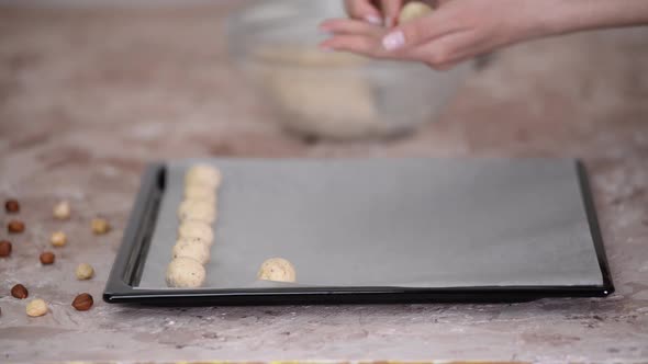A woman makes homemade shortbread dough cookies on the kitchen table and rolls balls.