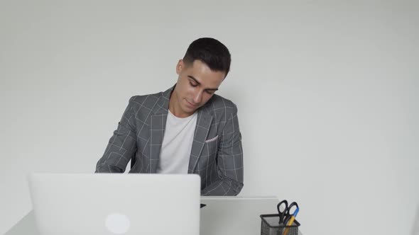 Handsome Male Student in a Suit Studies on a Laptop at Table Remotely Indoors alt