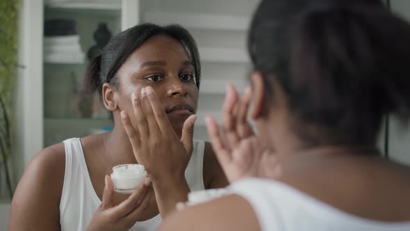 Young African-American  woman applying face cream in the mirror reflection. Shot with RED helium cam alt