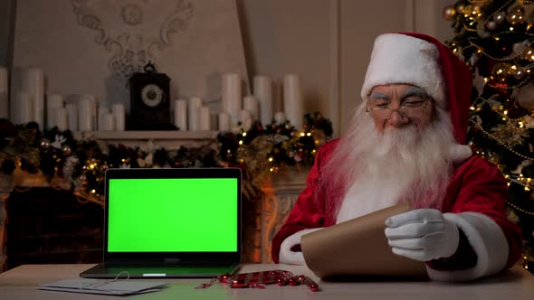 Smiling Santa Claus Reading Letter with List of Gifts Laptop Green Screen alt