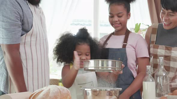 Happy African American family enjoy sifting the bread flour for Family day in holiday alt