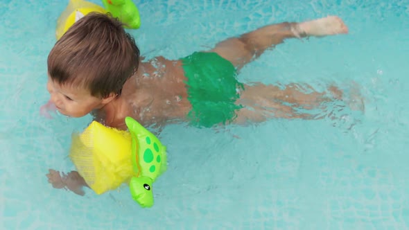 Kid in Oversleeves Swims in the Pool in the Yard alt