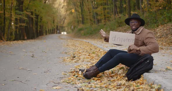 Black Hitchhiker with a Sign in Hands on the Roadside alt